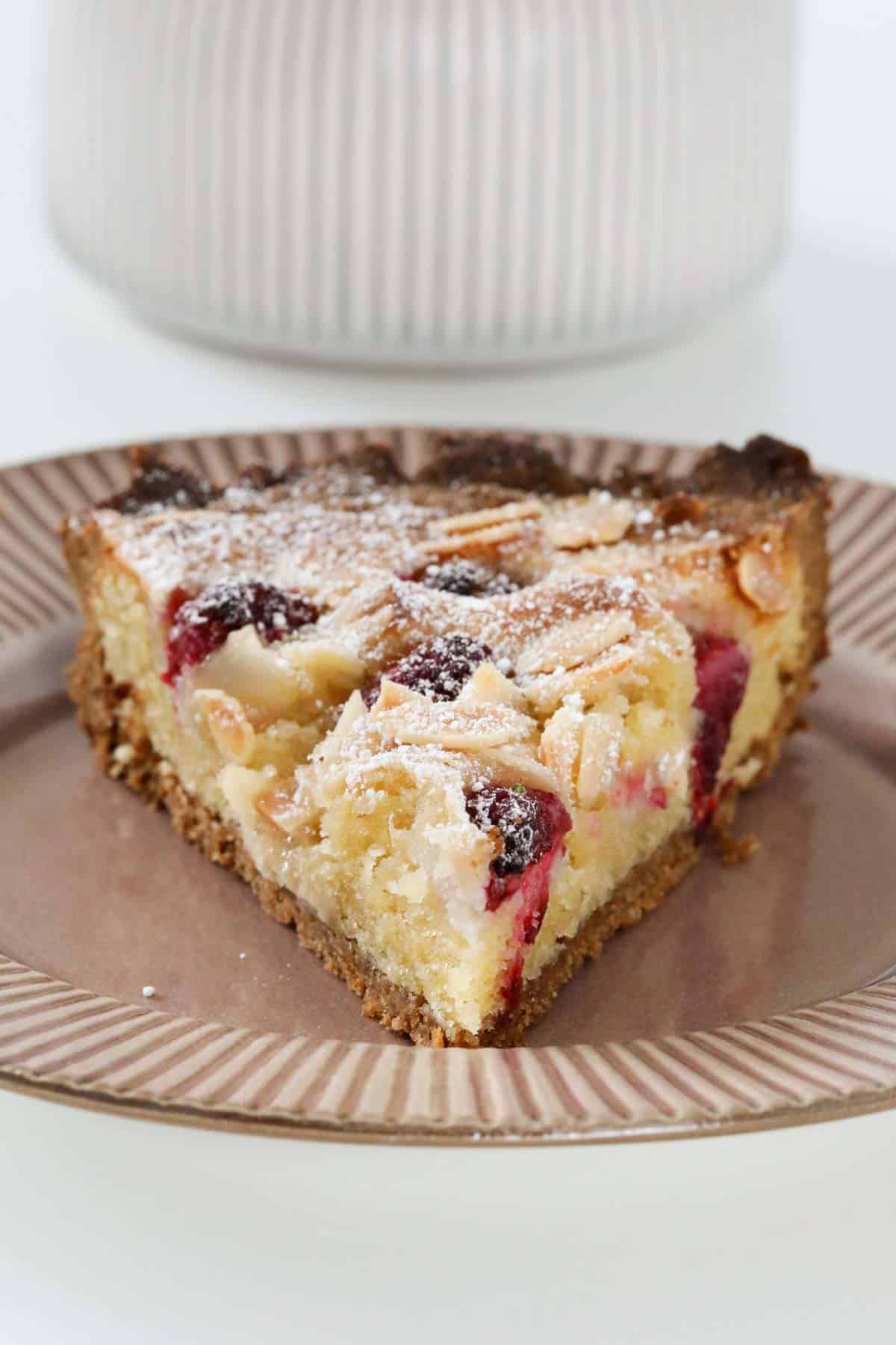A brown plate with a slice of raspberry frangipane tart on it.
