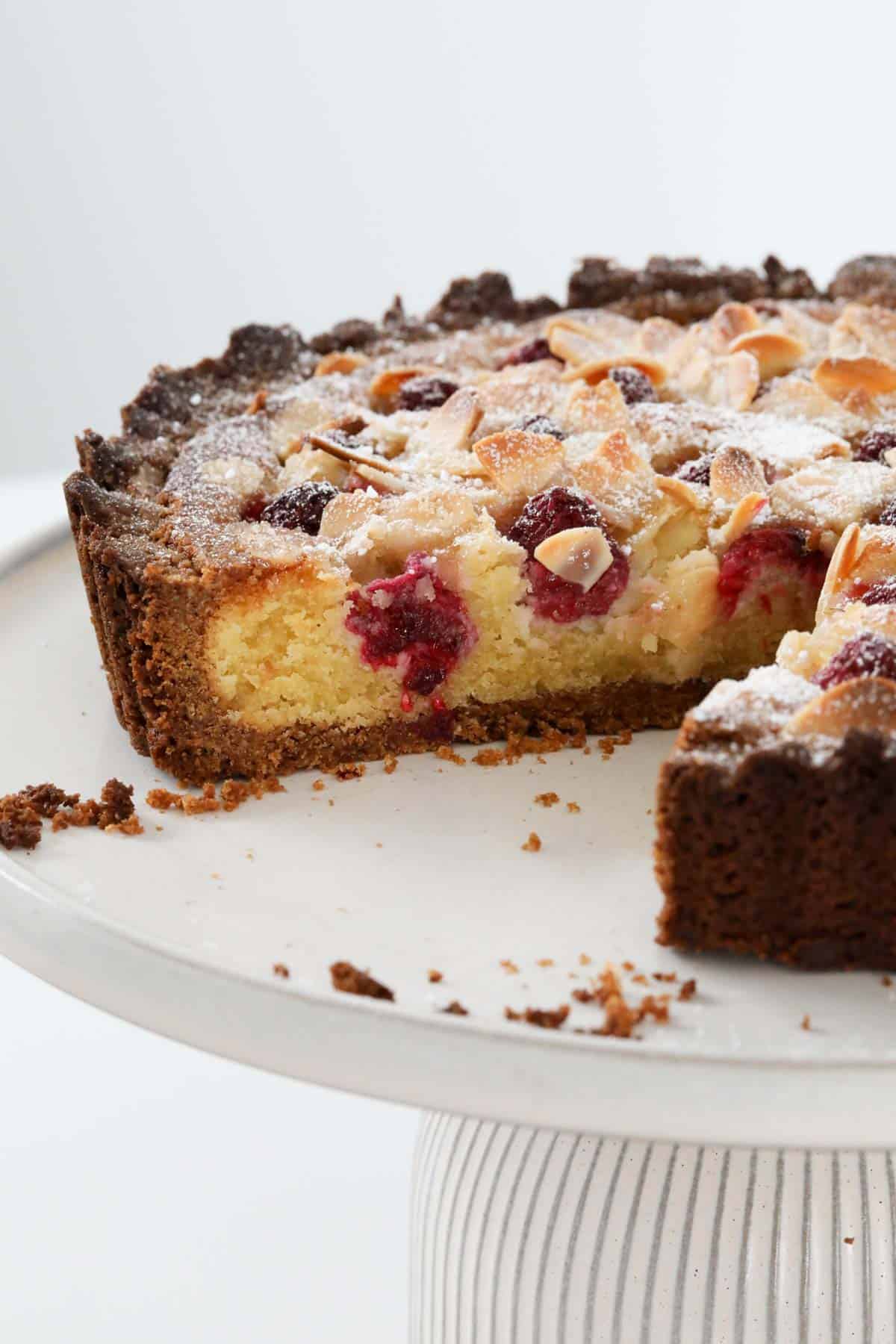 A raspberry and almond dessert cake on a cake stand with one serve removed.