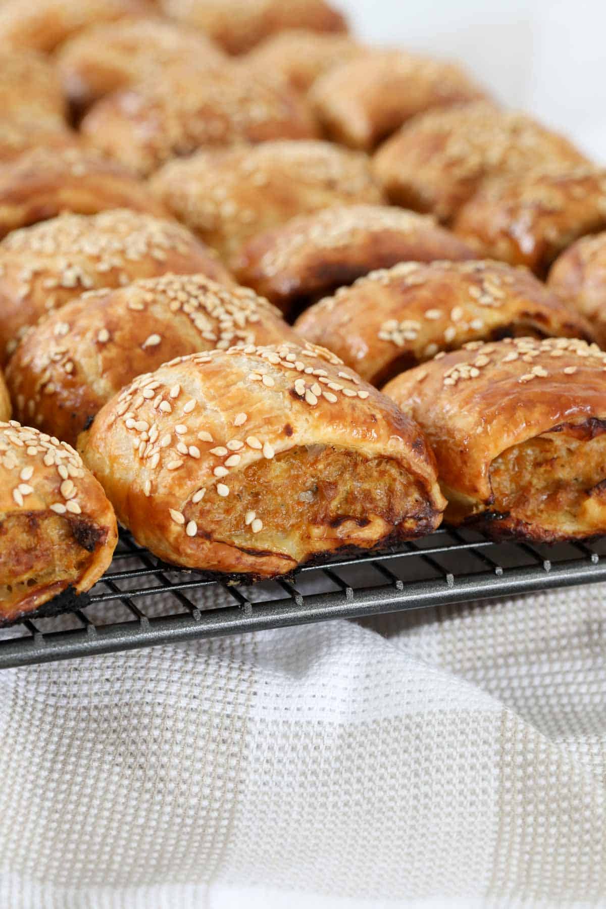 Sausage rolls encased in puff pastry cooling on a wire rack. 