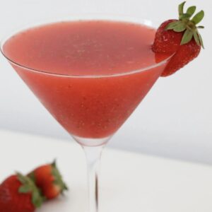 A glass of a strawberry martini with a strawberry as a garnish.