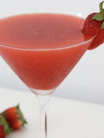 A glass of a strawberry martini with a strawberry as a garnish.