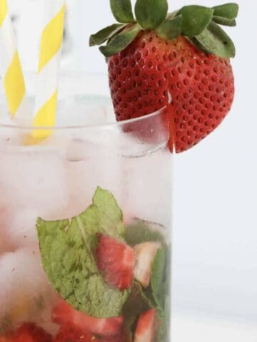 A glass filled with a mojito cocktail with strawberries.