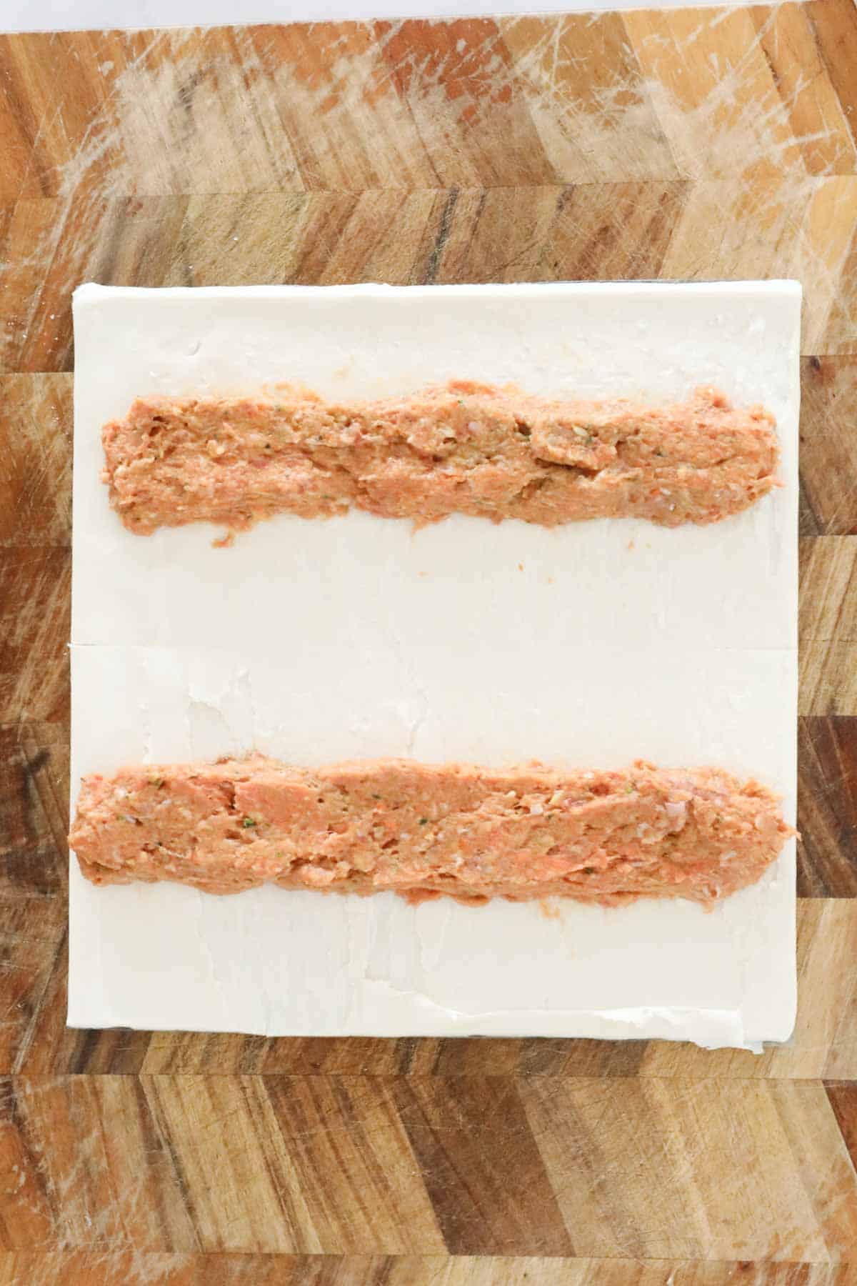 Pork mince mix placed in two long lines on a pastry sheet cut in half.