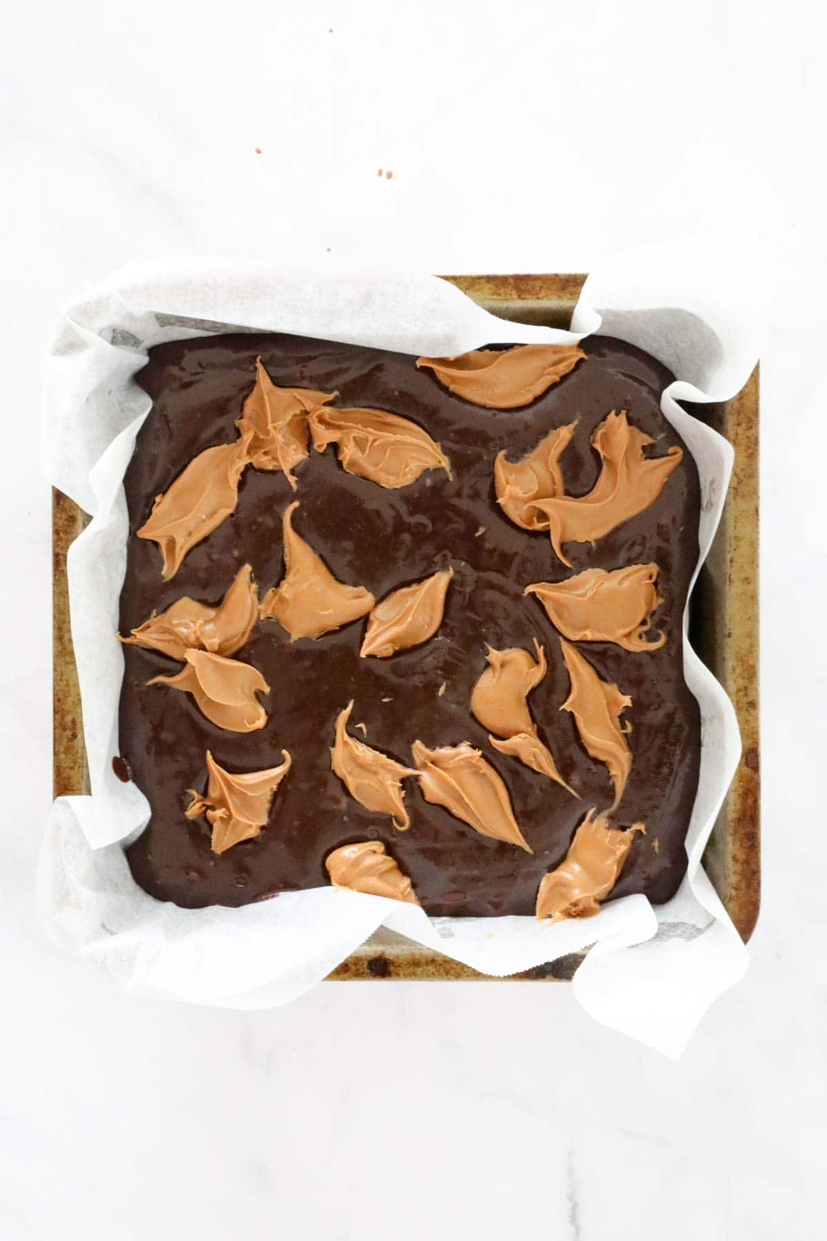 Dollops of Biscoff spread placed over the top of slice mix in a lined baking tin.