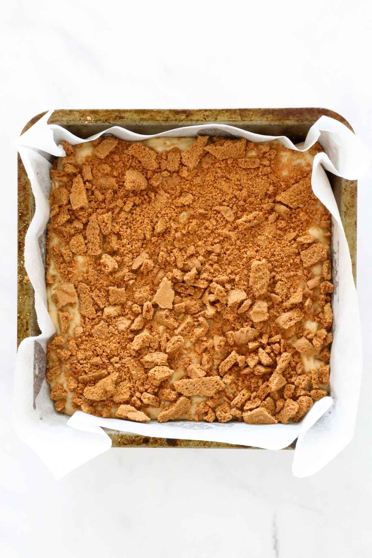 Mixture spread into a paper lined tray, with more cookie crumbs sprinkled over the top.