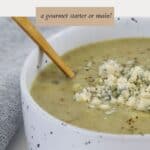 A white speckled bowl filled with broccoli soup and blue cheese crumbled over the top.