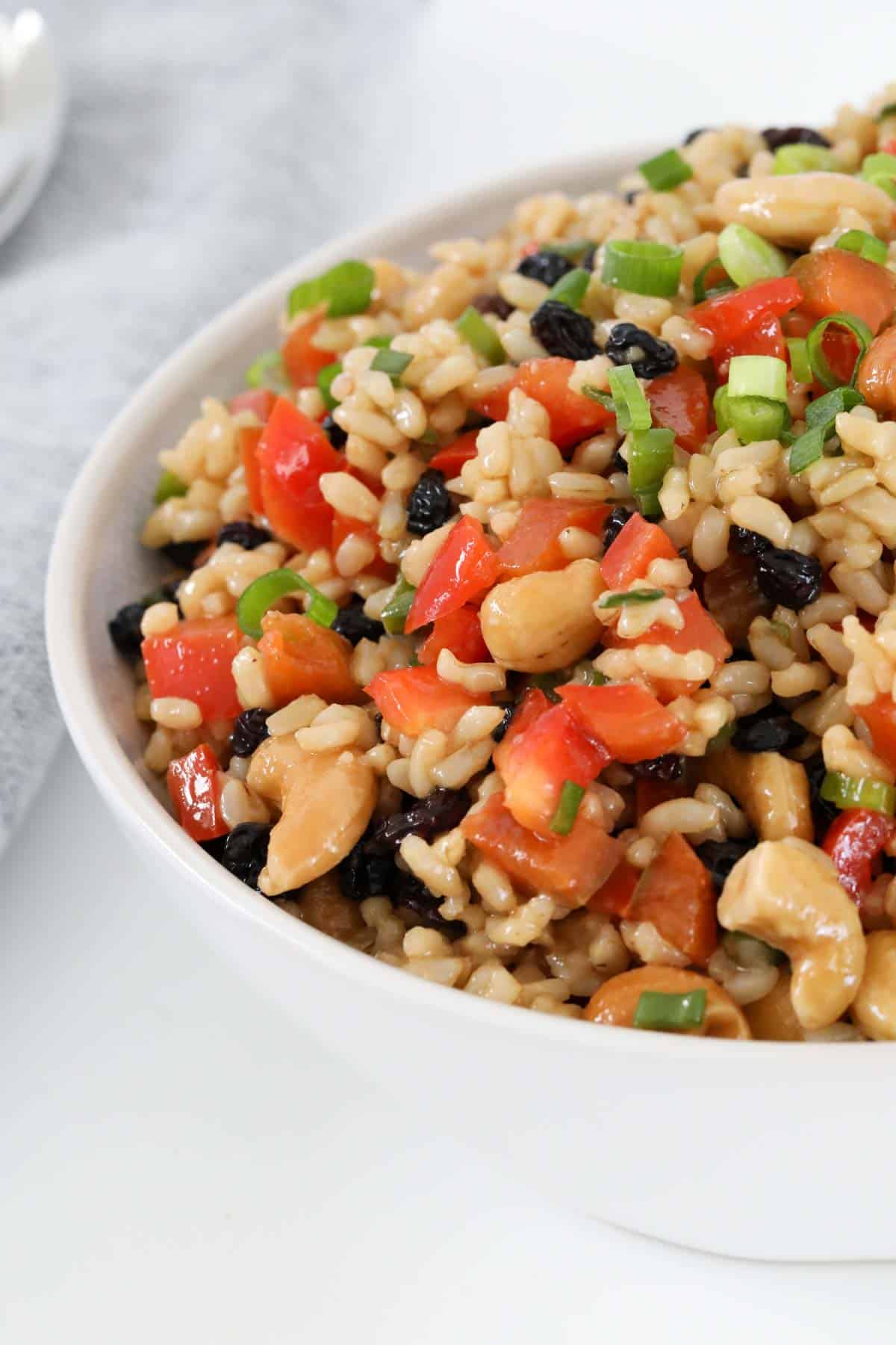 A white serving bowl of brown rice salad with cashews and currants.