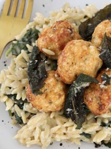 A plate of golden baked chicken meatballs on a bed of creamy risoni with sage leaves.