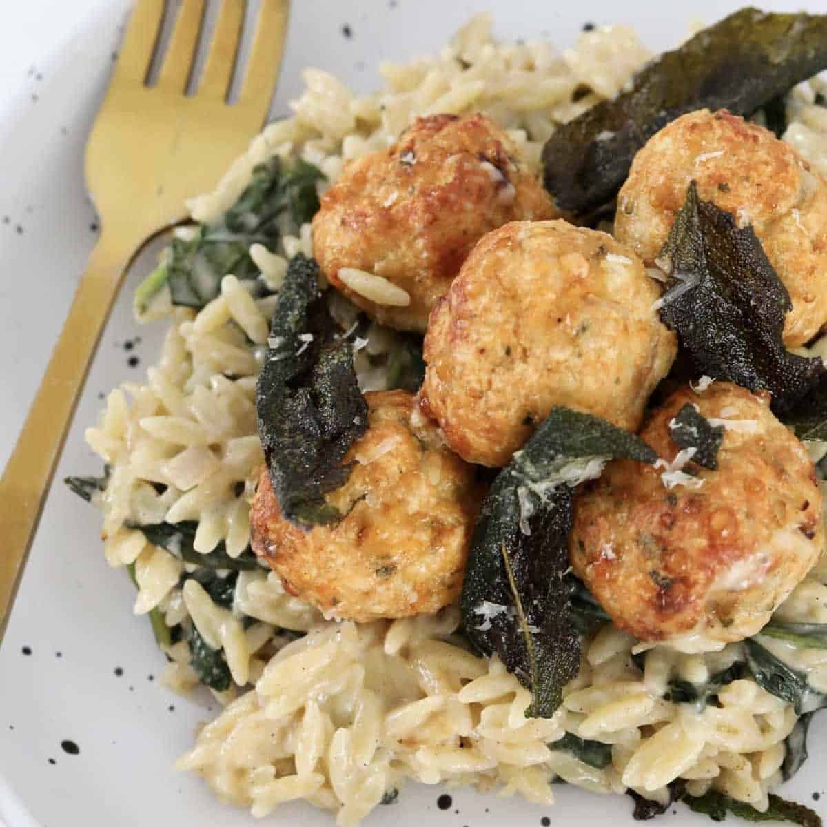 A plate of golden baked chicken meatballs on a bed of creamy risoni with sage leaves.