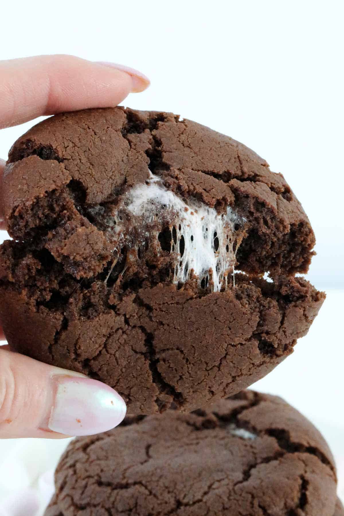 A hand breaking a chocolate cookie in half to show the chewy marshmallow centre.
