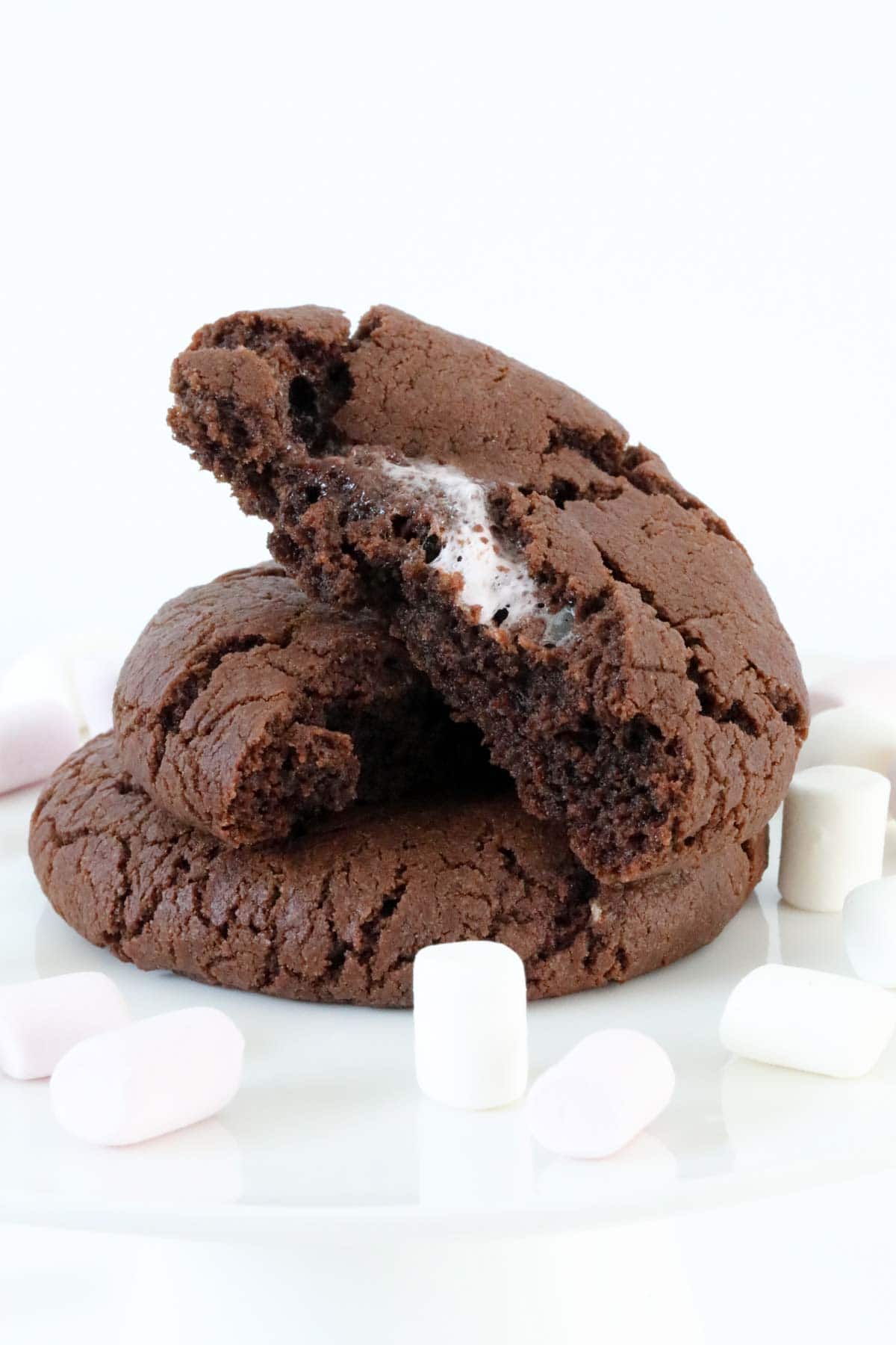 Two chocolate marshmallow cookies, the top one broken in half to show the marshmallow centre.