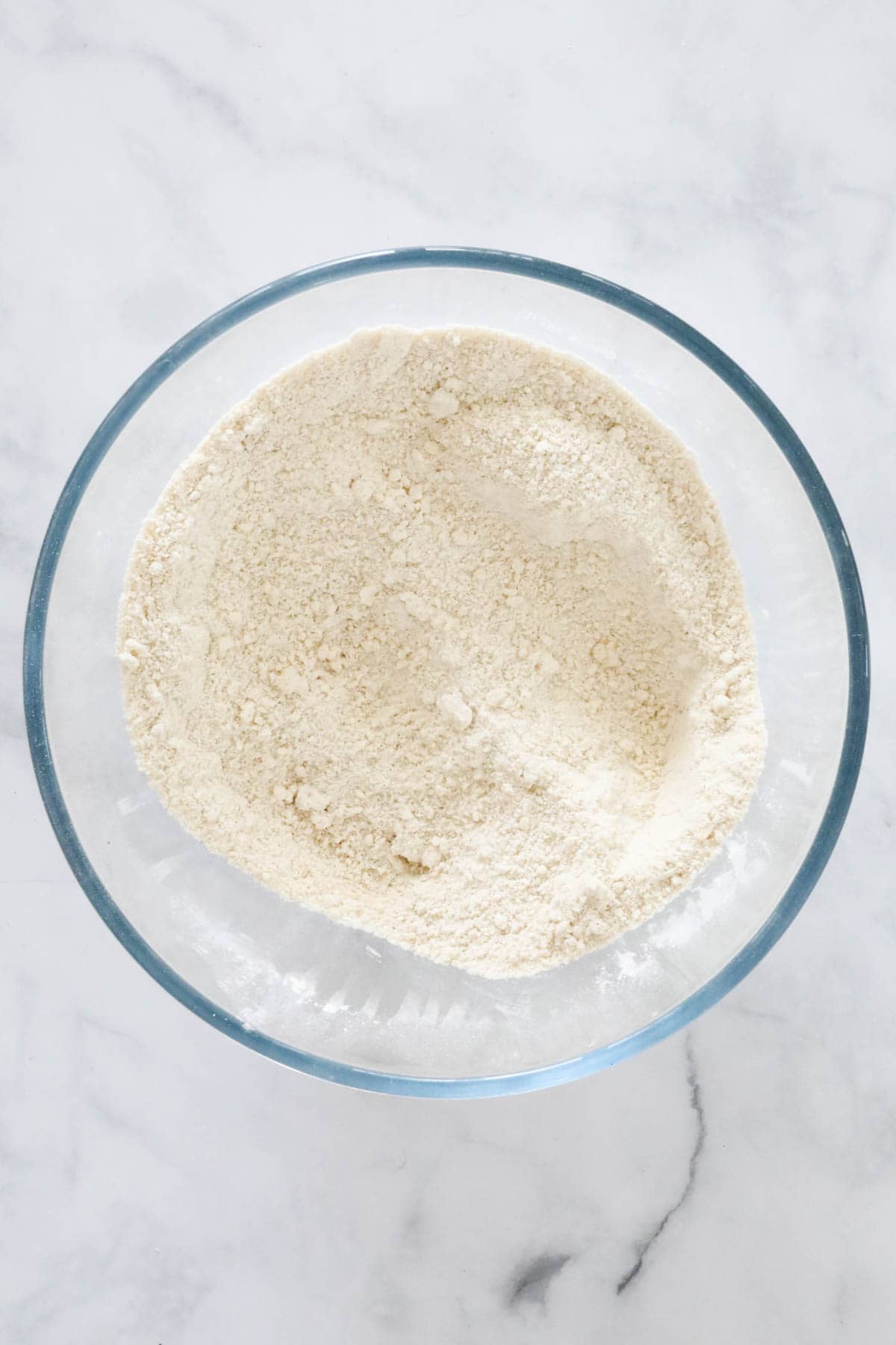 Dry ingredients mixed in a glass bowl, with a hollow made in the centre of the flour mix.