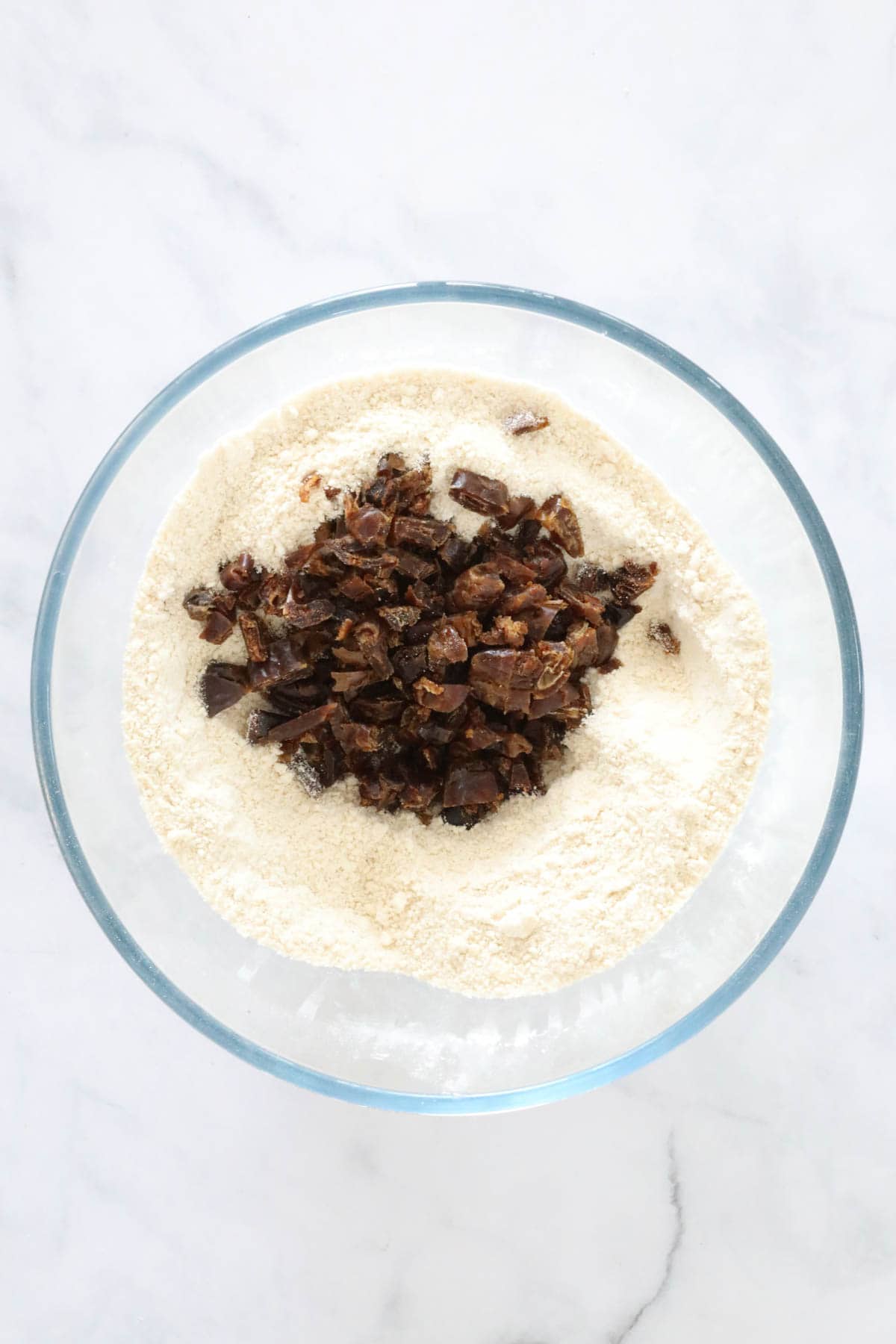 Chopped dates added to dry mix in a clear glass bowl.