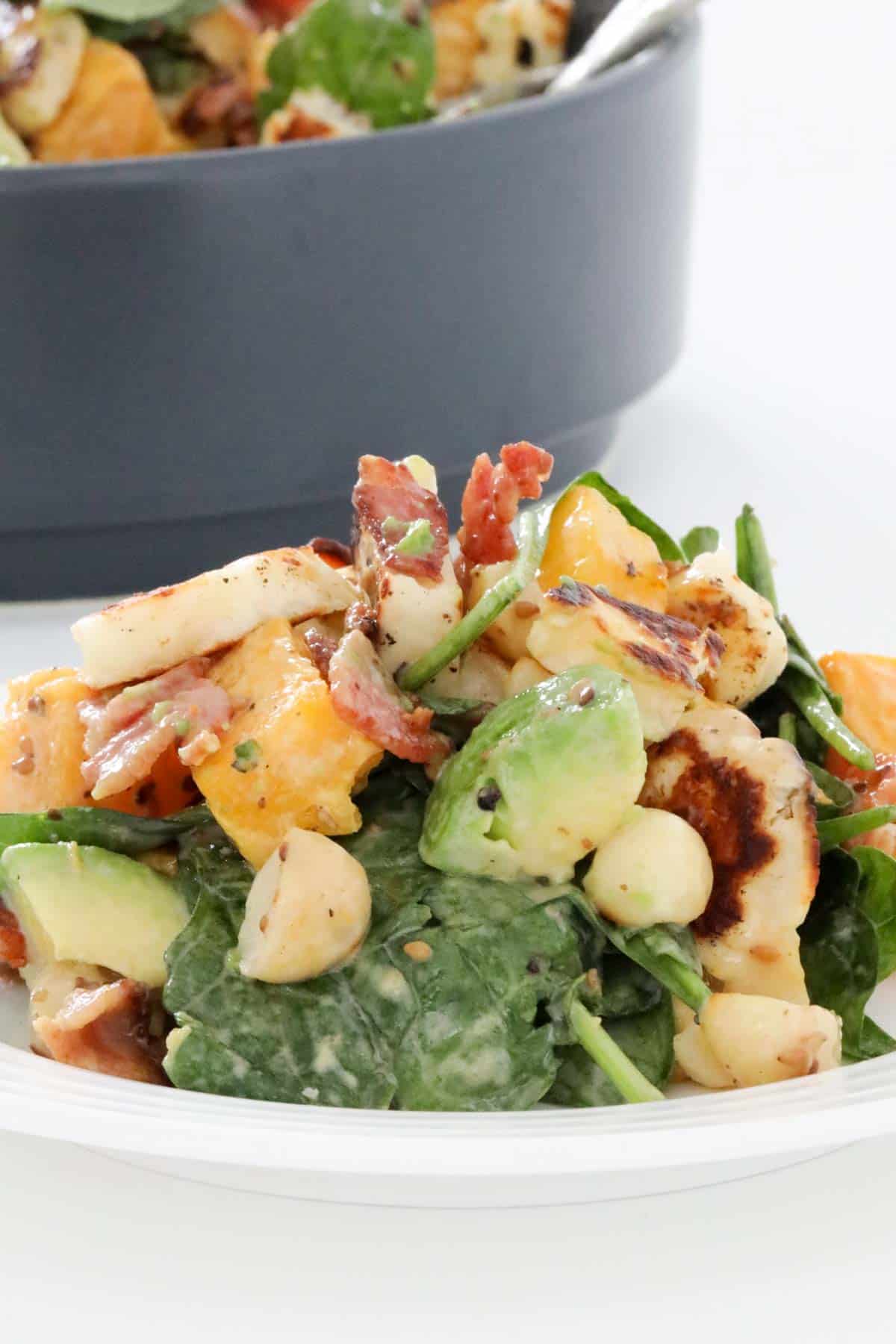 A plate of halloumi salad with bacon and pumpkin, with the serving bowl of salad just visible behind.
