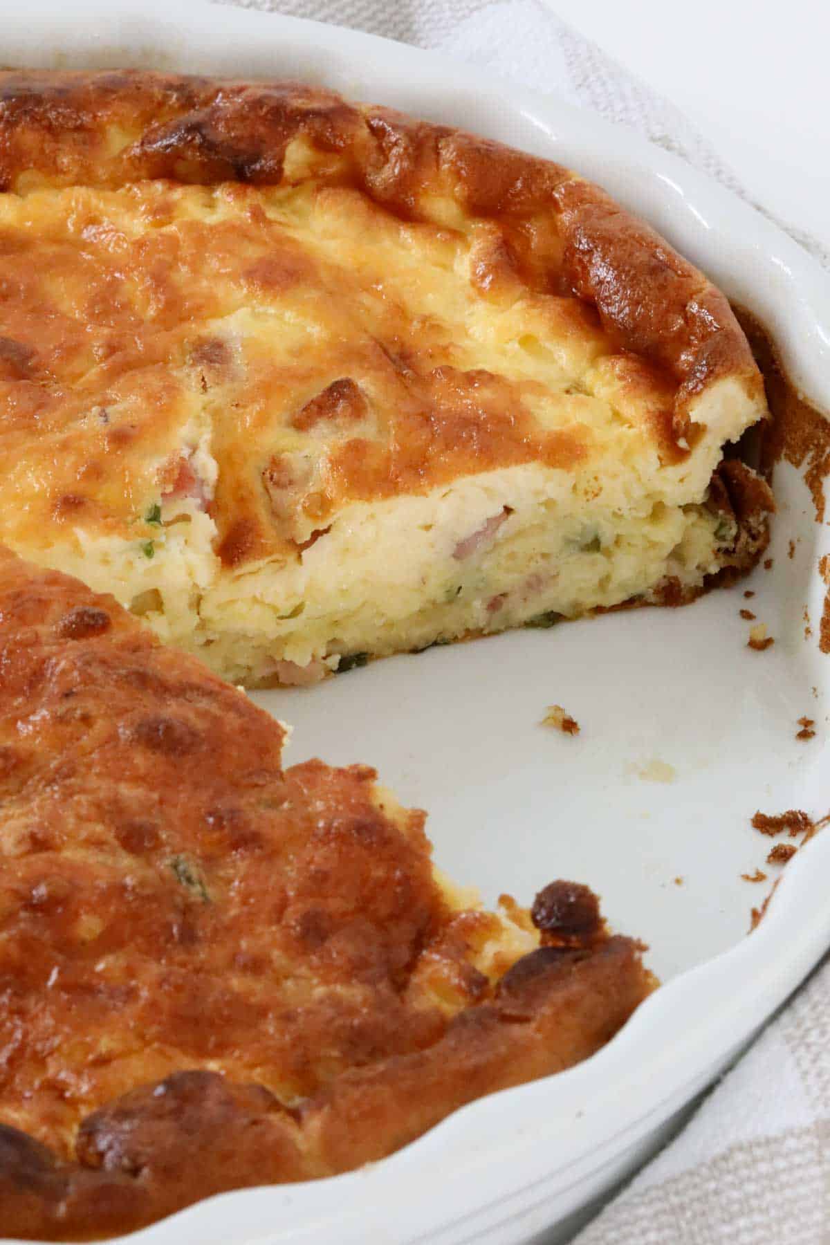 A golden baked impossible quiche in a baking dish with one piece removed.