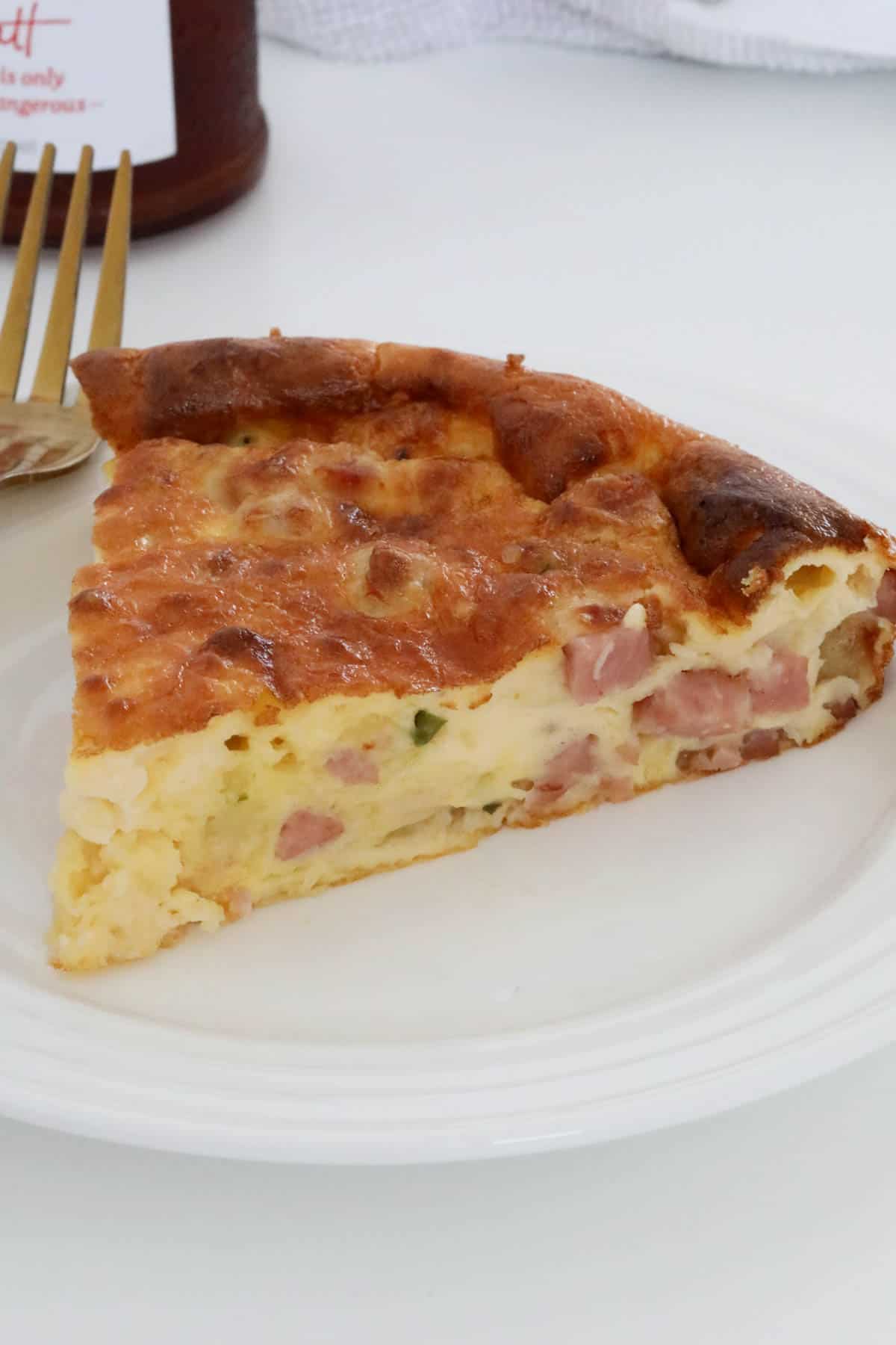 A triangle of egg quiche showing a filling of bacon and chives, served on a white plate.