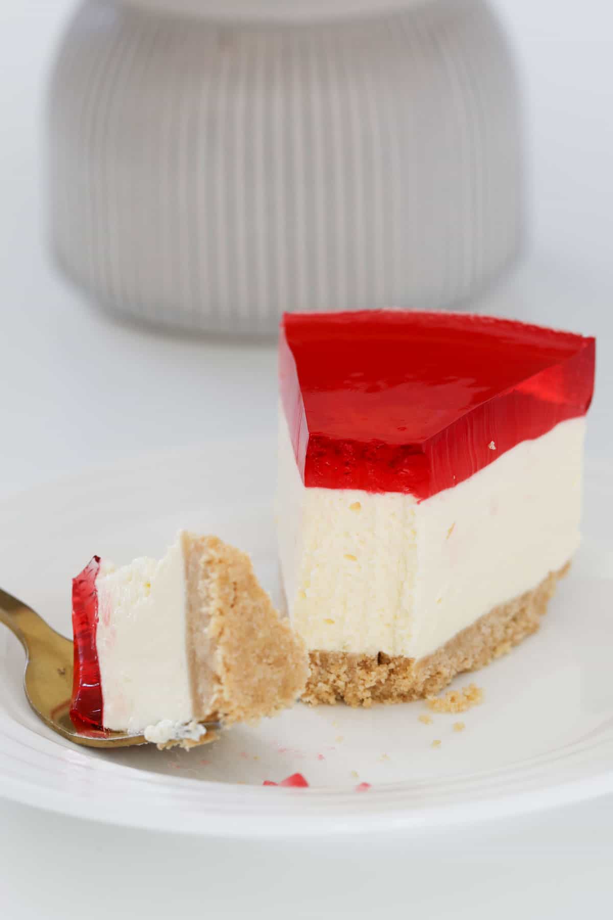 A slice of cheesecake on a plate being eaten with a fork.