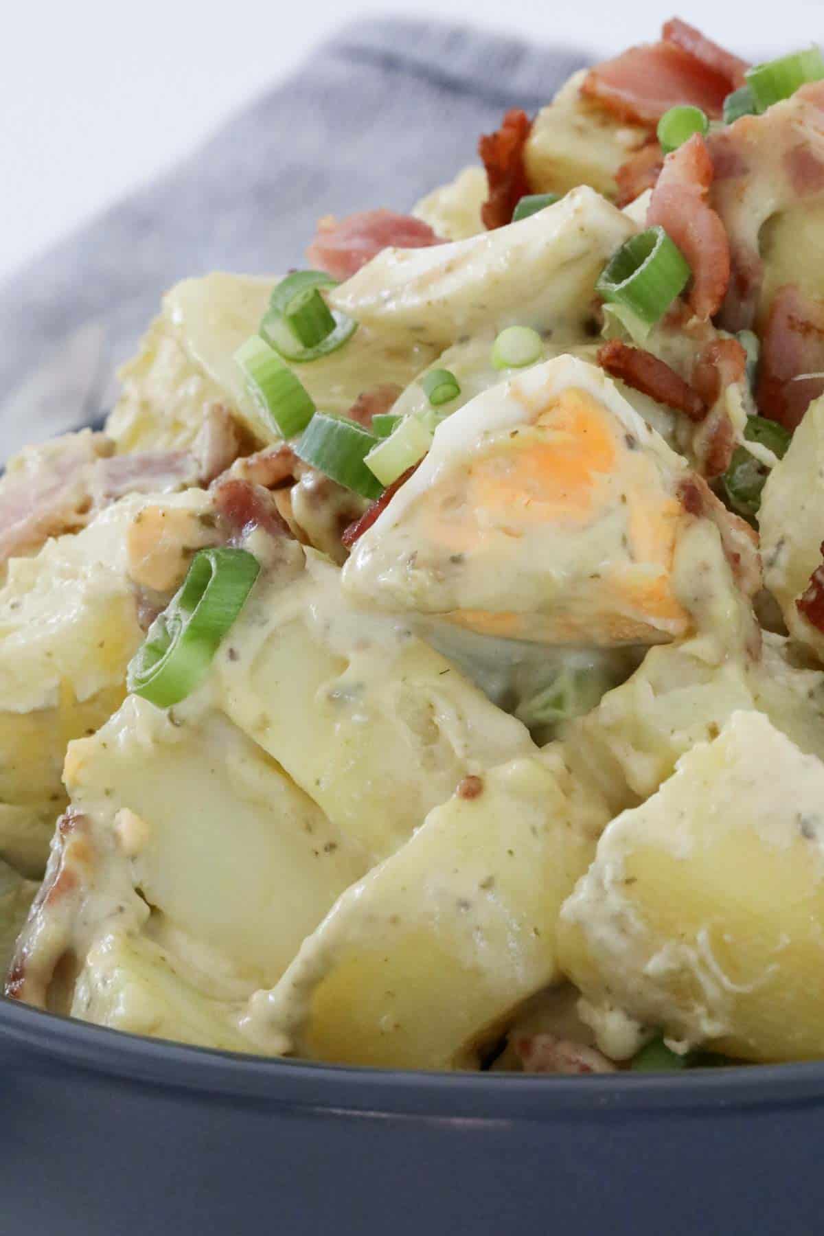 Close up of a dish of pesto potato salad with boiled eggs and bacon.