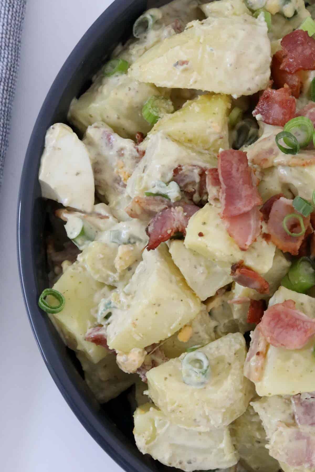 Pesto potato salad in a serving bowl with crispy diced bacon and spring onions on top.