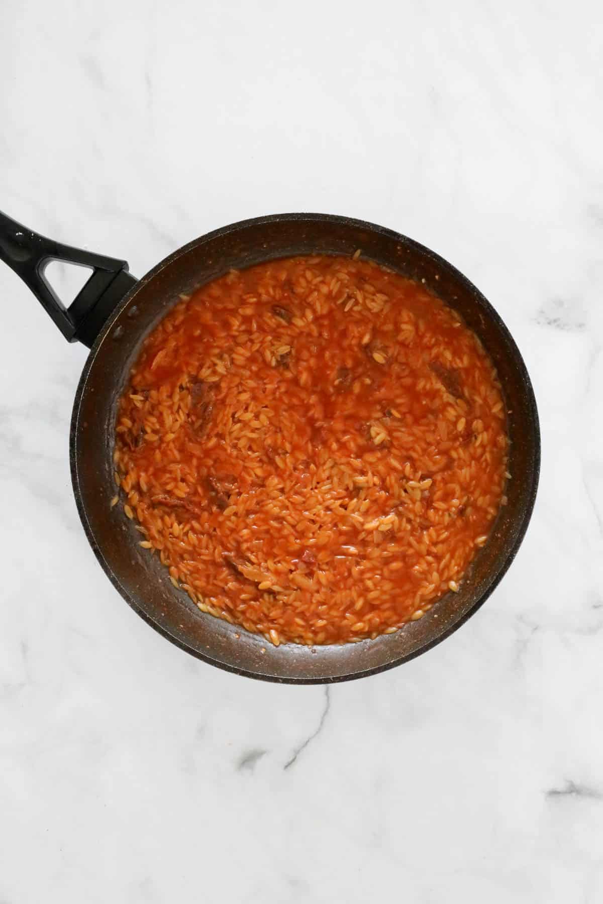 The cooked tomato risoni in a frying pan.