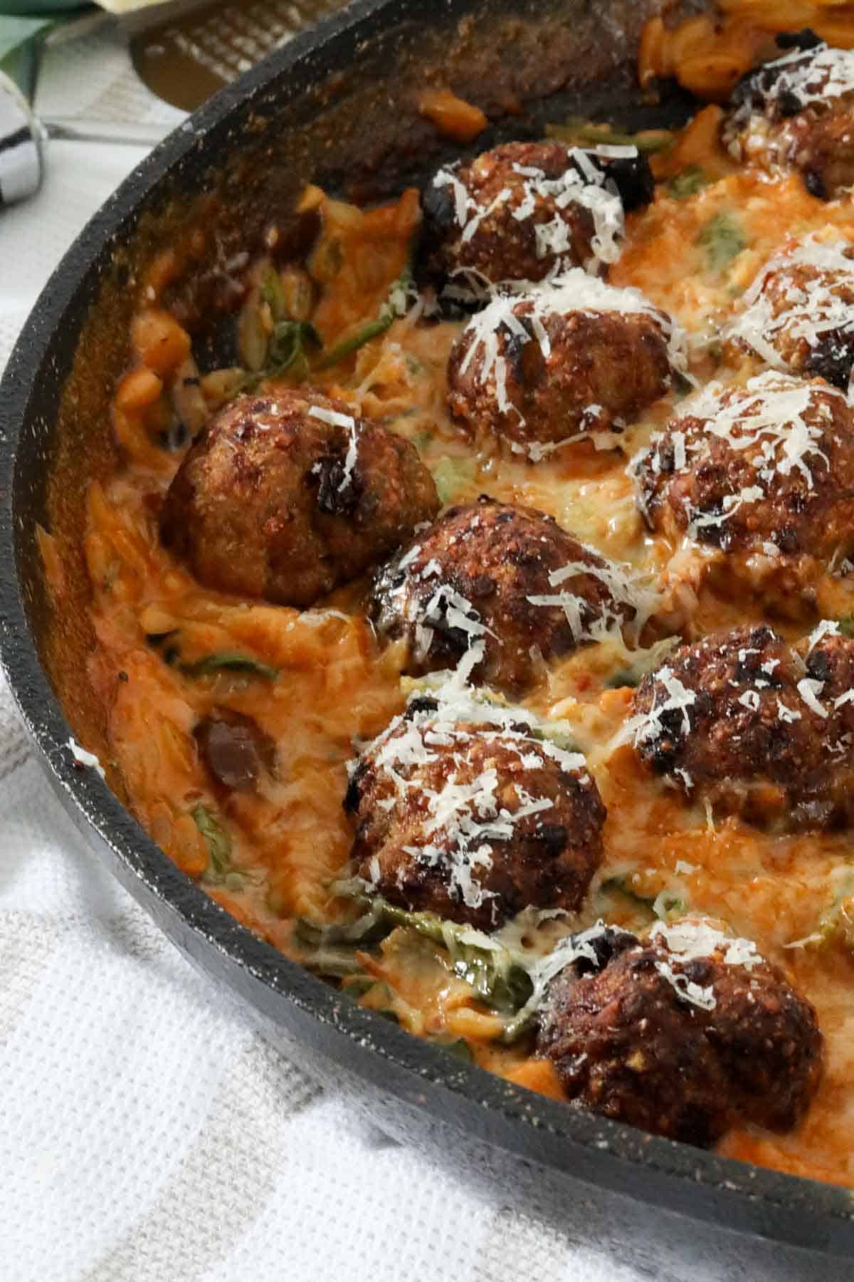 Cooked meatballs and risoni in the pan, sprinkled with grated parmesan.