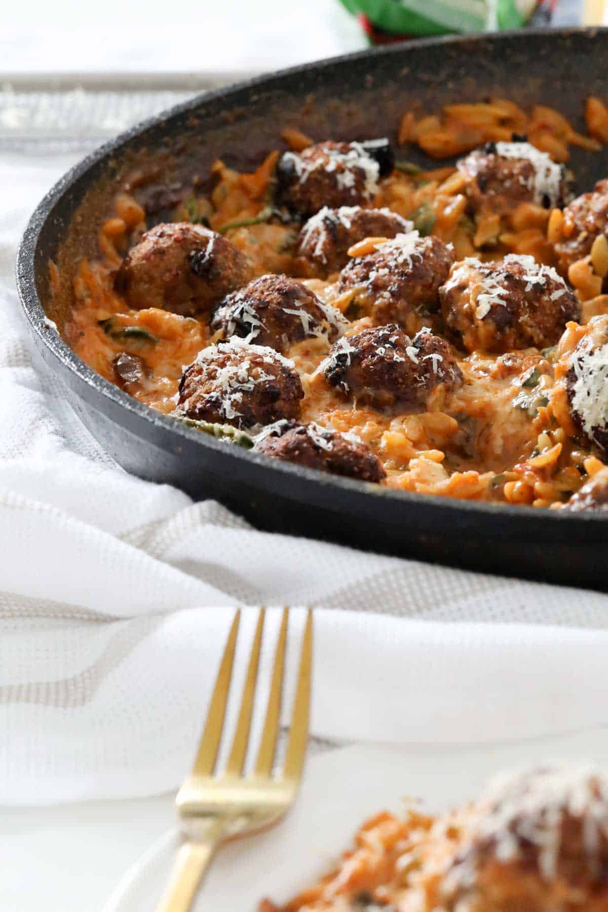 A frying pan filled with meatballs on top of creamy risoni.