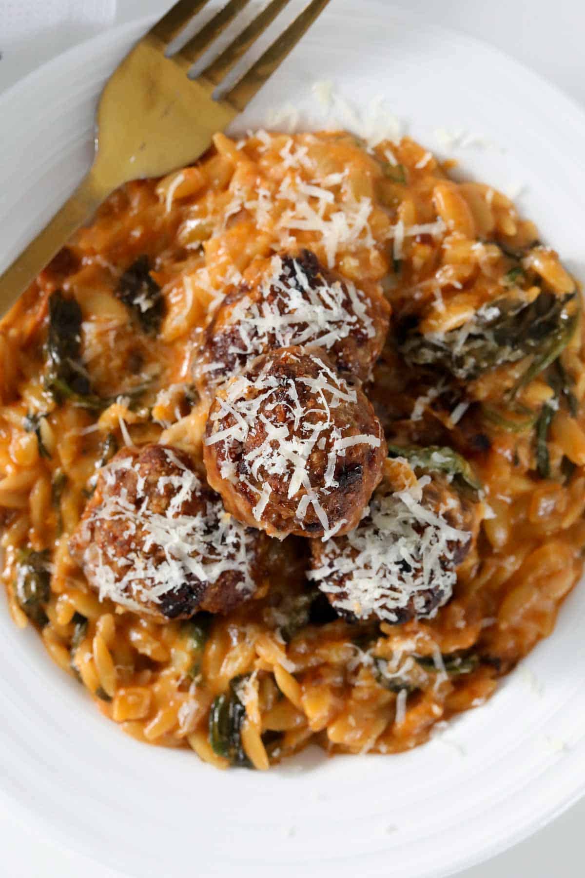 A white plate of baked pork meatballs and creamy tomato risoni.