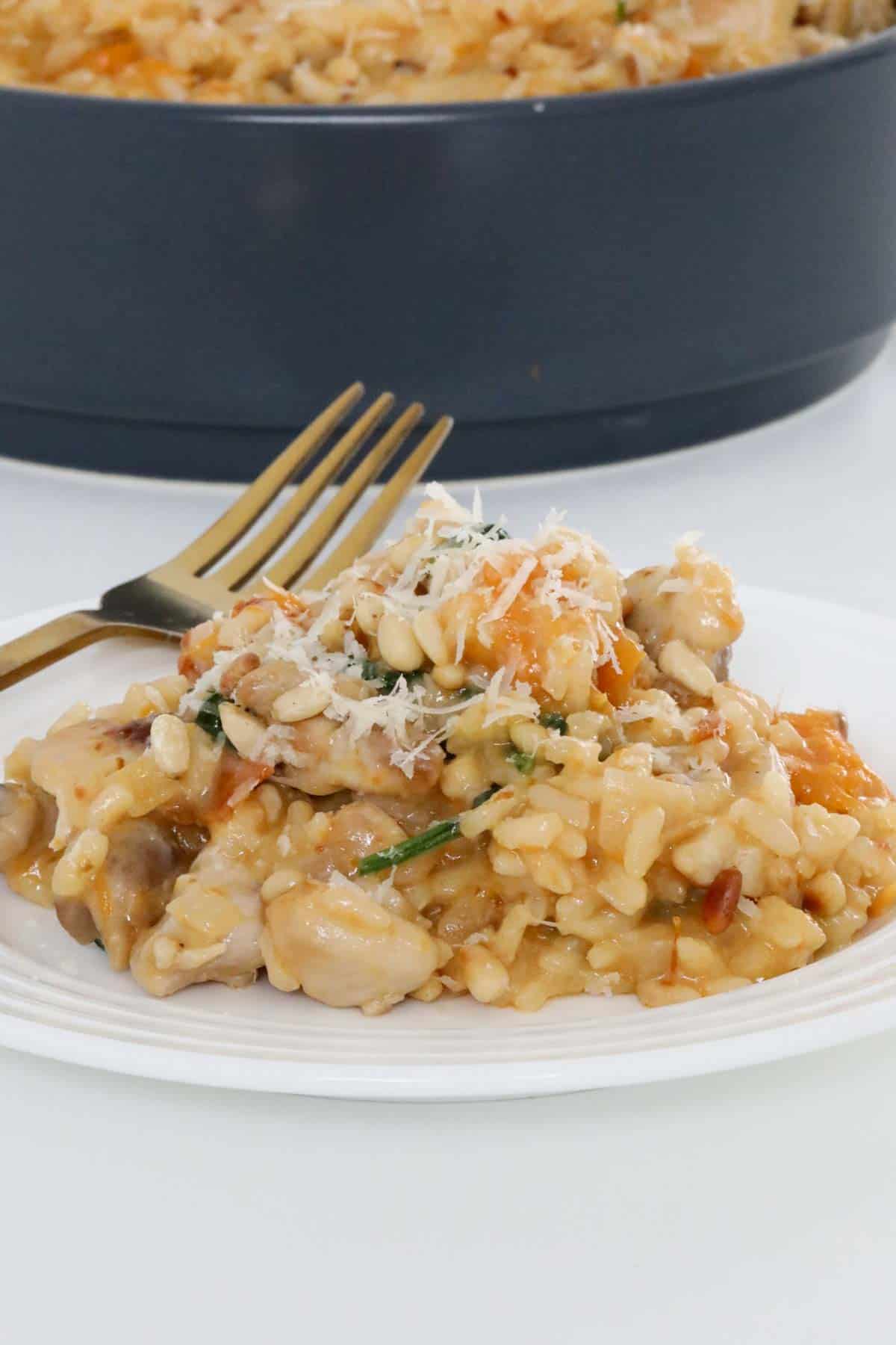 A plate of risotto with a fork, the serving dish of risotto just visible behind.