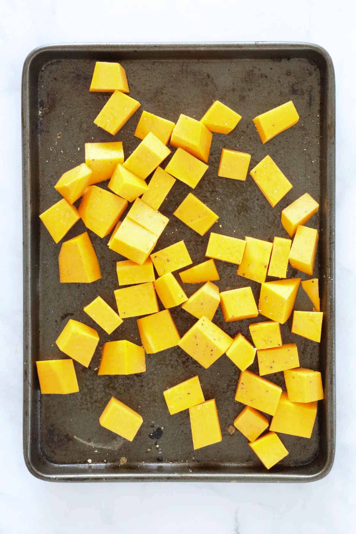 Cubes of pumpkin on a baking tray drizzled with oil, salt and pepper ready to roast.