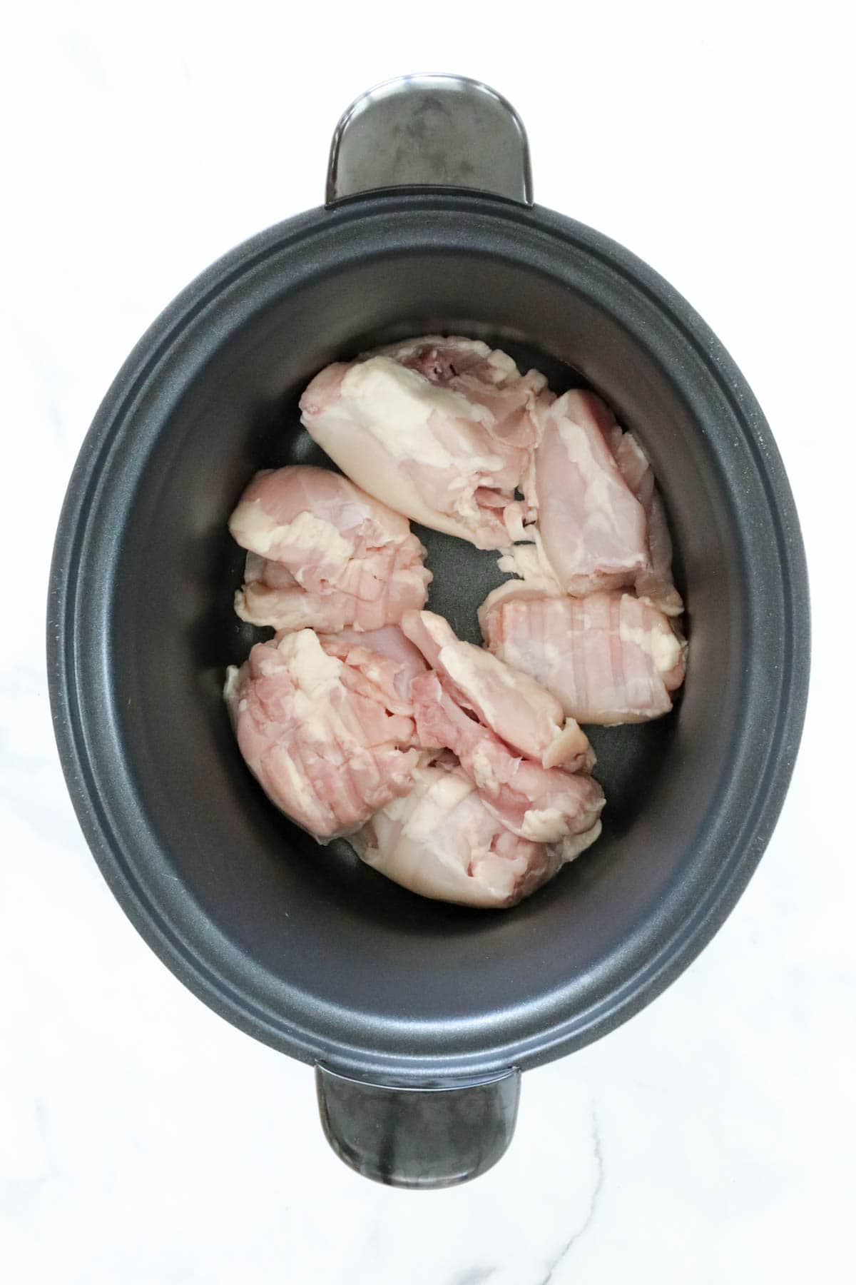 Chicken thigh fillets in the base of a crockpot.