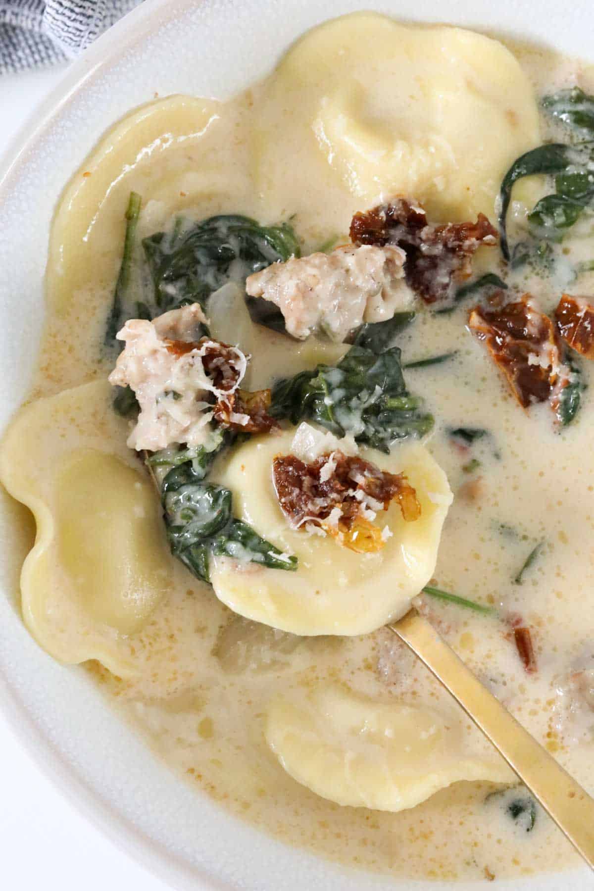 A bowl of creamy Tuscan sausage soup with a spoon holding up a portion of it.
