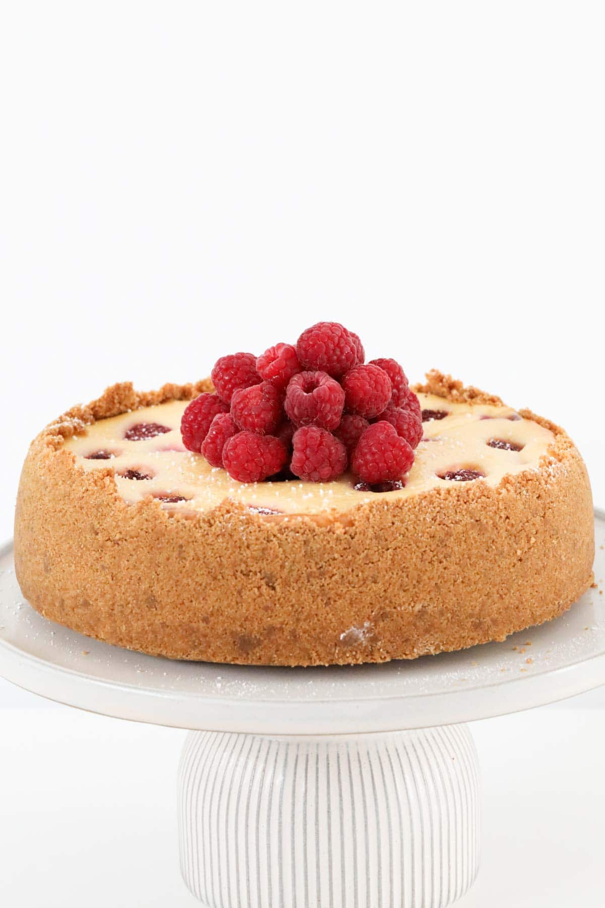 A raspberry baked cheesecake on a white cake stand.