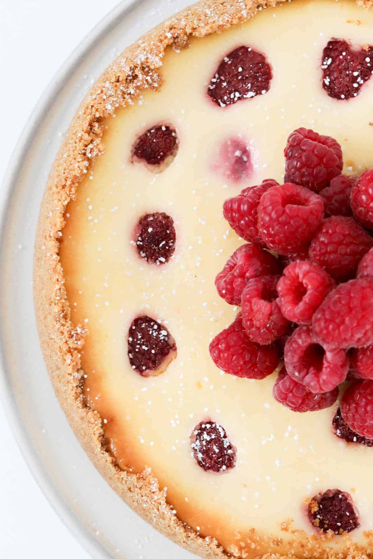 Overhead shot of baked cheesecake with a pile of fresh raspberries on top.