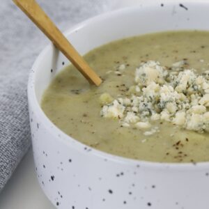 A bowl of broccoli and blue cheese soup with extra blue cheese crumbled on top.
