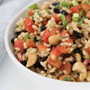 A bowl of brown rice salad with cashews, capsicum and currants.