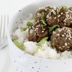 A bowl of beef meatballs with marinade on rice.