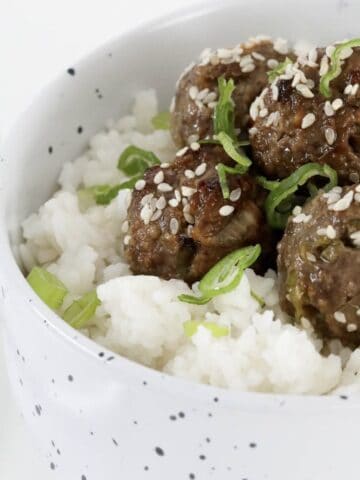 A bowl of beef meatballs with marinade on rice.