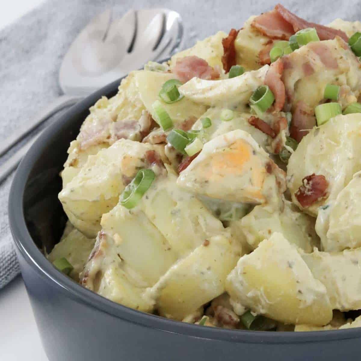 A bowl of pesto potato salad with crispy bacon and eggs.