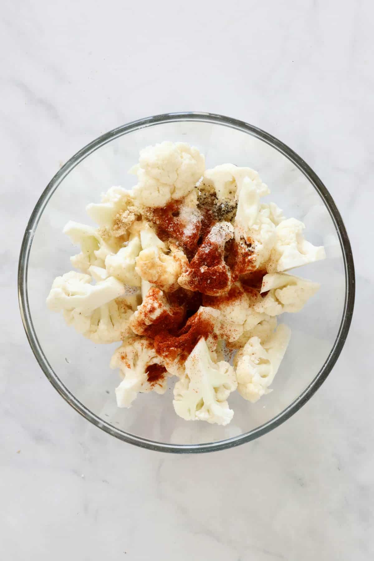 Cauliflower florets in a bowl sprinkled with the seasonings.