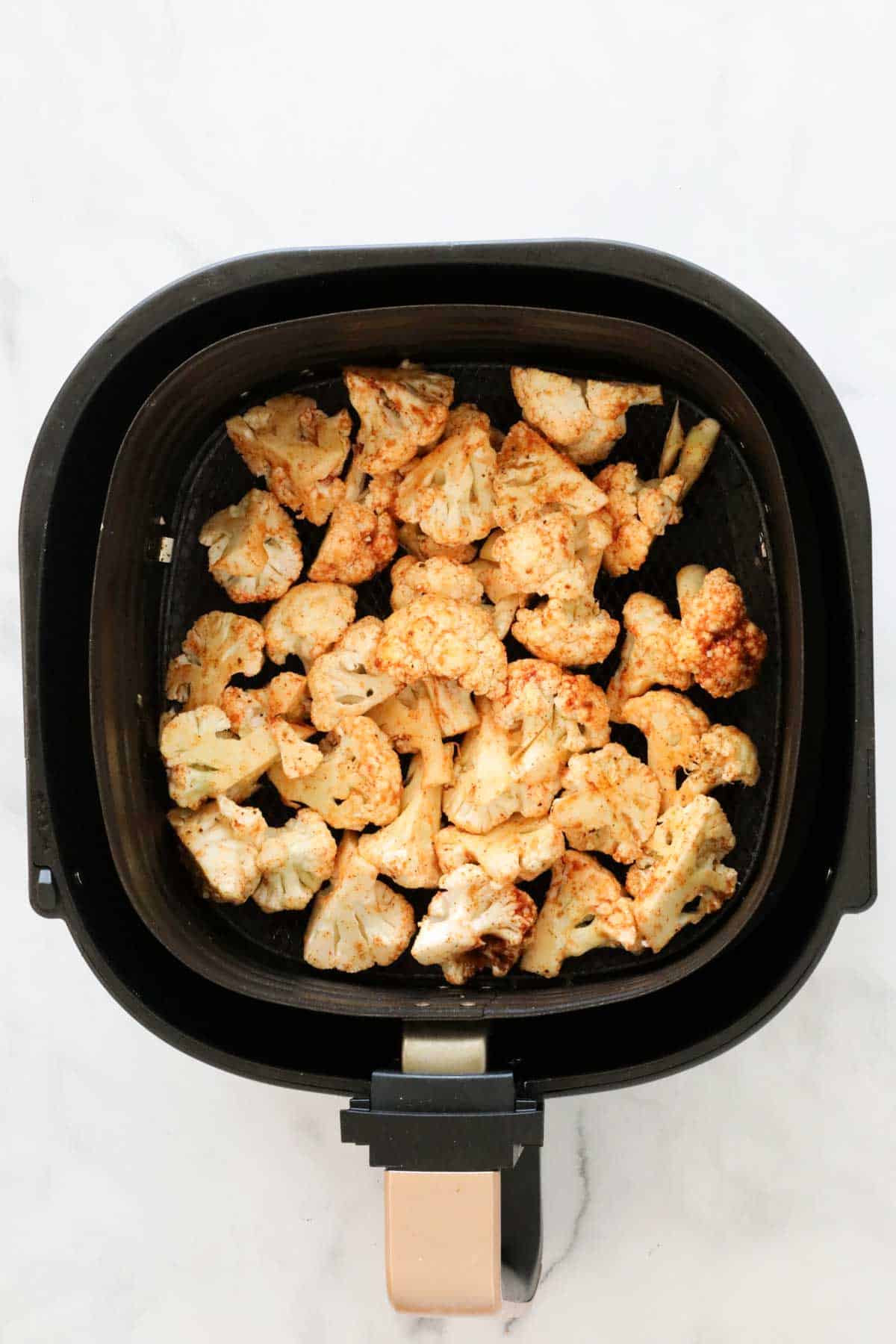 The cauliflower in the pan of an air fryer.
