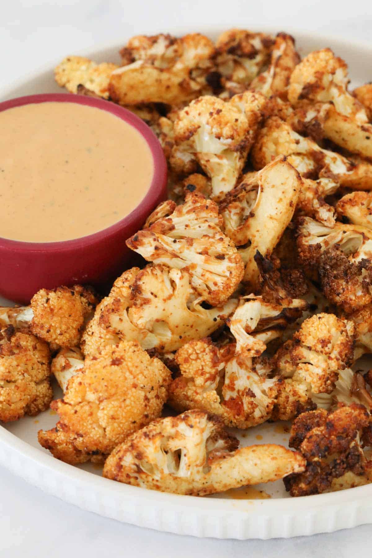 A white plate of air fryer cauliflower served with dip.