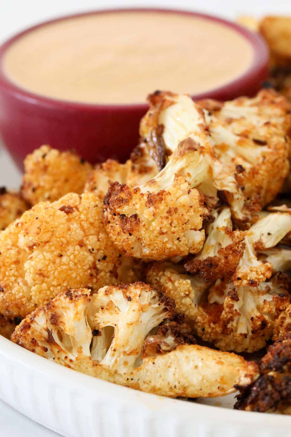 A plate of crispy air fryer cauliflower with a bowl of dip in the background.