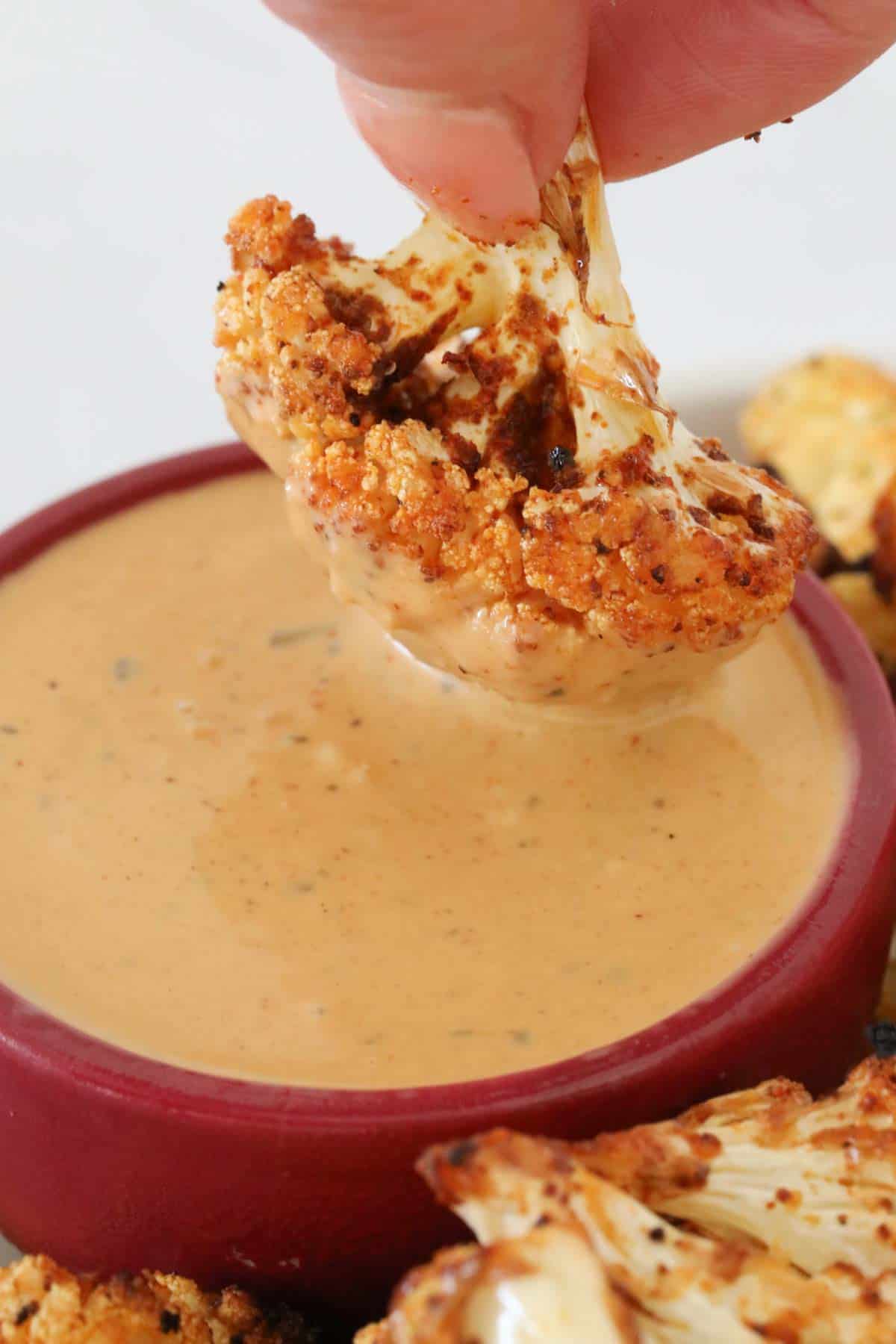 An air fried cauliflower floret being dipped in sauce.