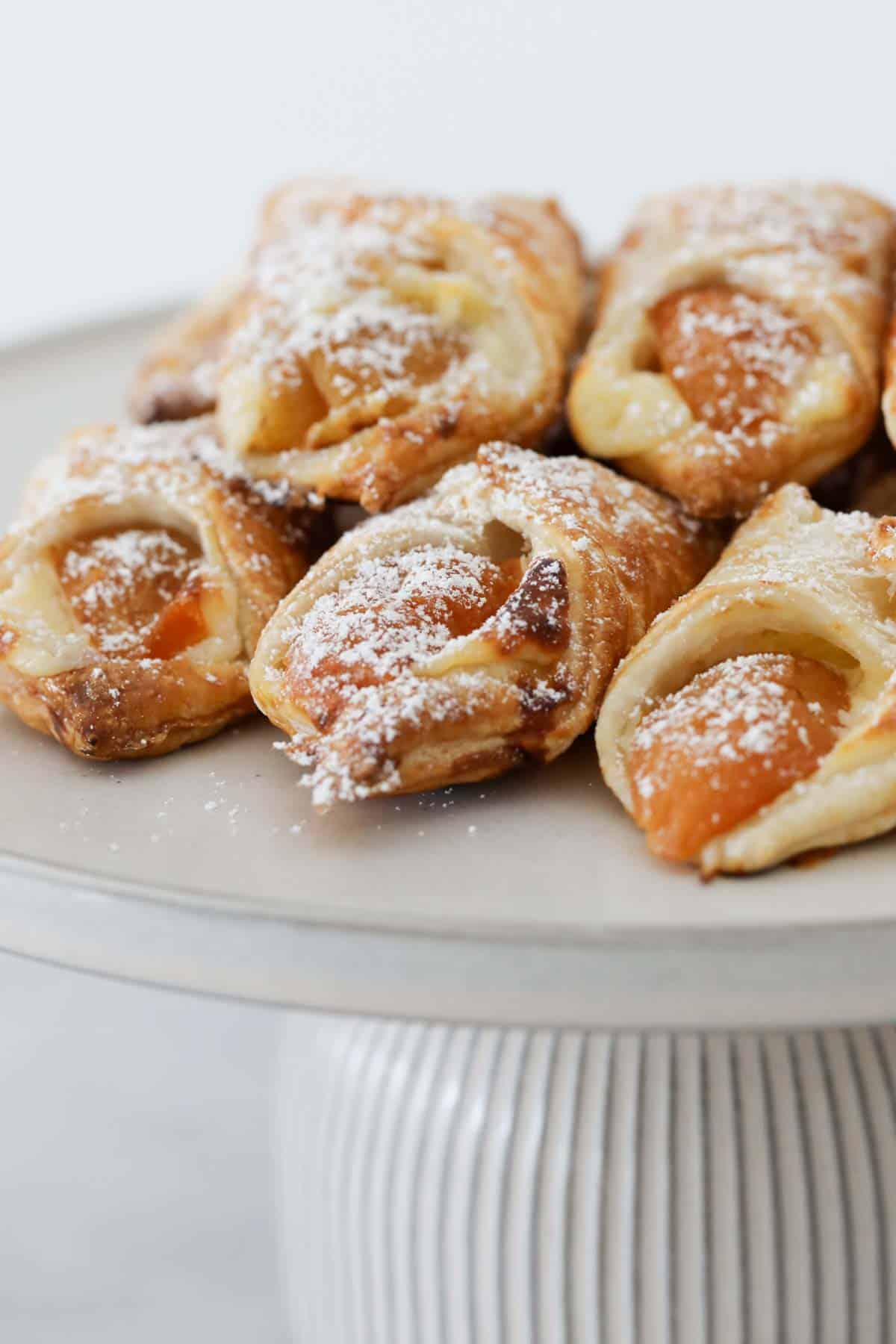 A pile of mini danishes, dusted with icing sugar and served on a cake tray.