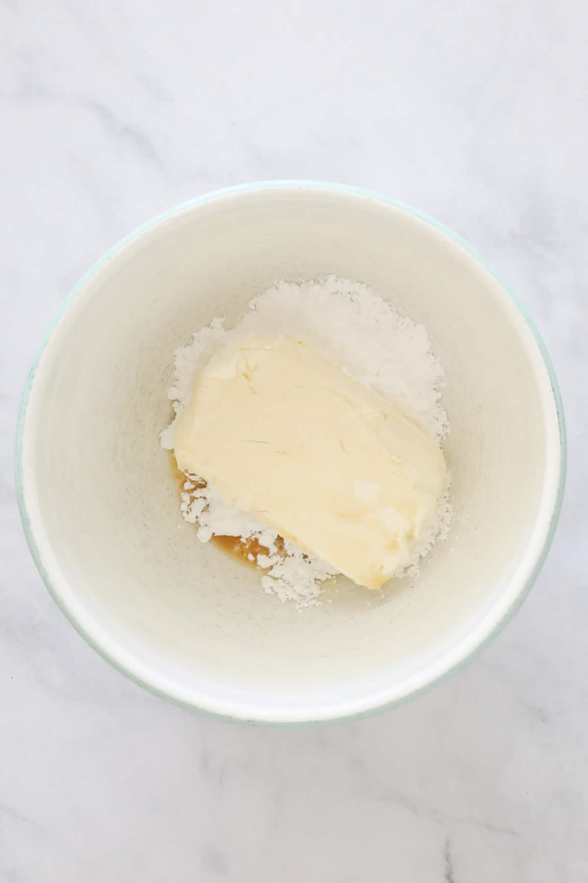 Cream cheese, icing sugar and vanilla extract in a white mixing bowl.