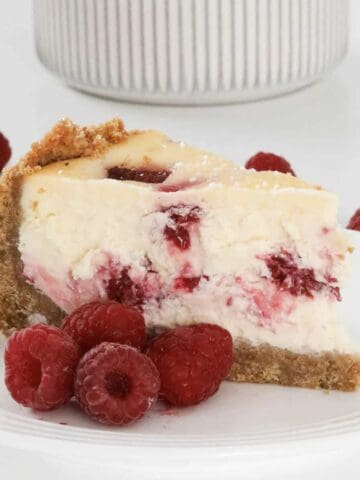 A serve of raspberry baked cheesecake with fresh raspberries beside it.