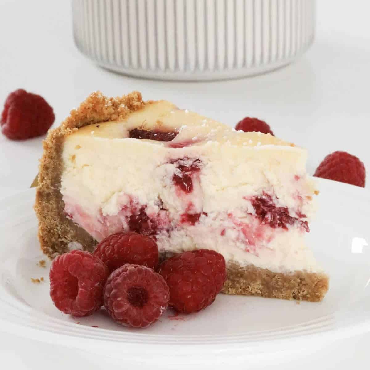 A serve of raspberry baked cheesecake with fresh raspberries beside it.