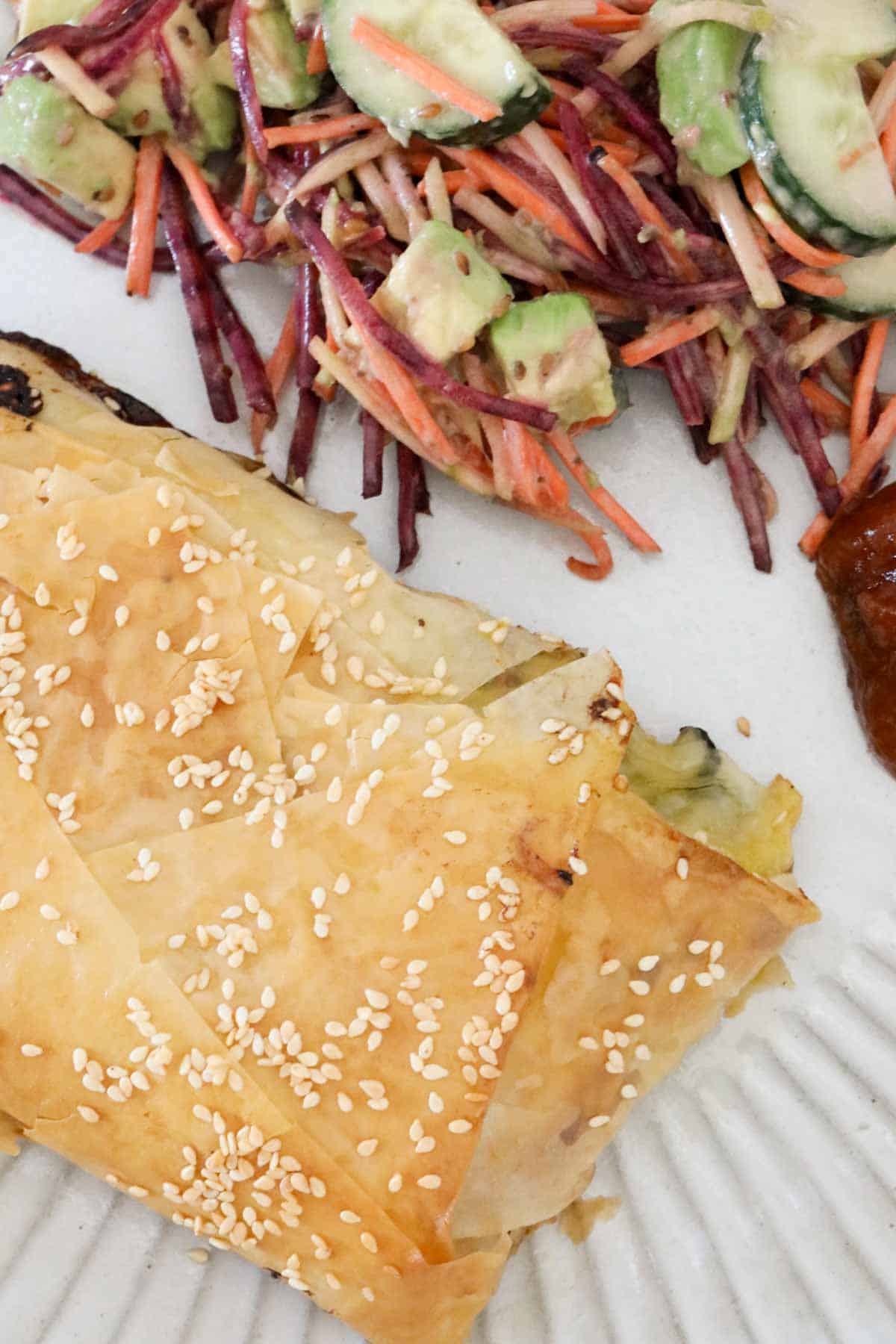 A baked chicken filo parcel, sprinkled with sesame seeds, served on a plate served with coleslaw.