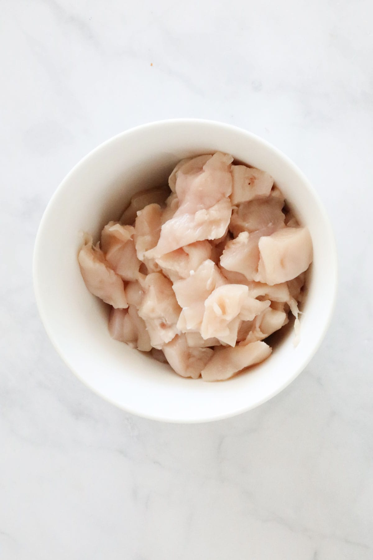 Chopped chicken breasts in a white bowl.