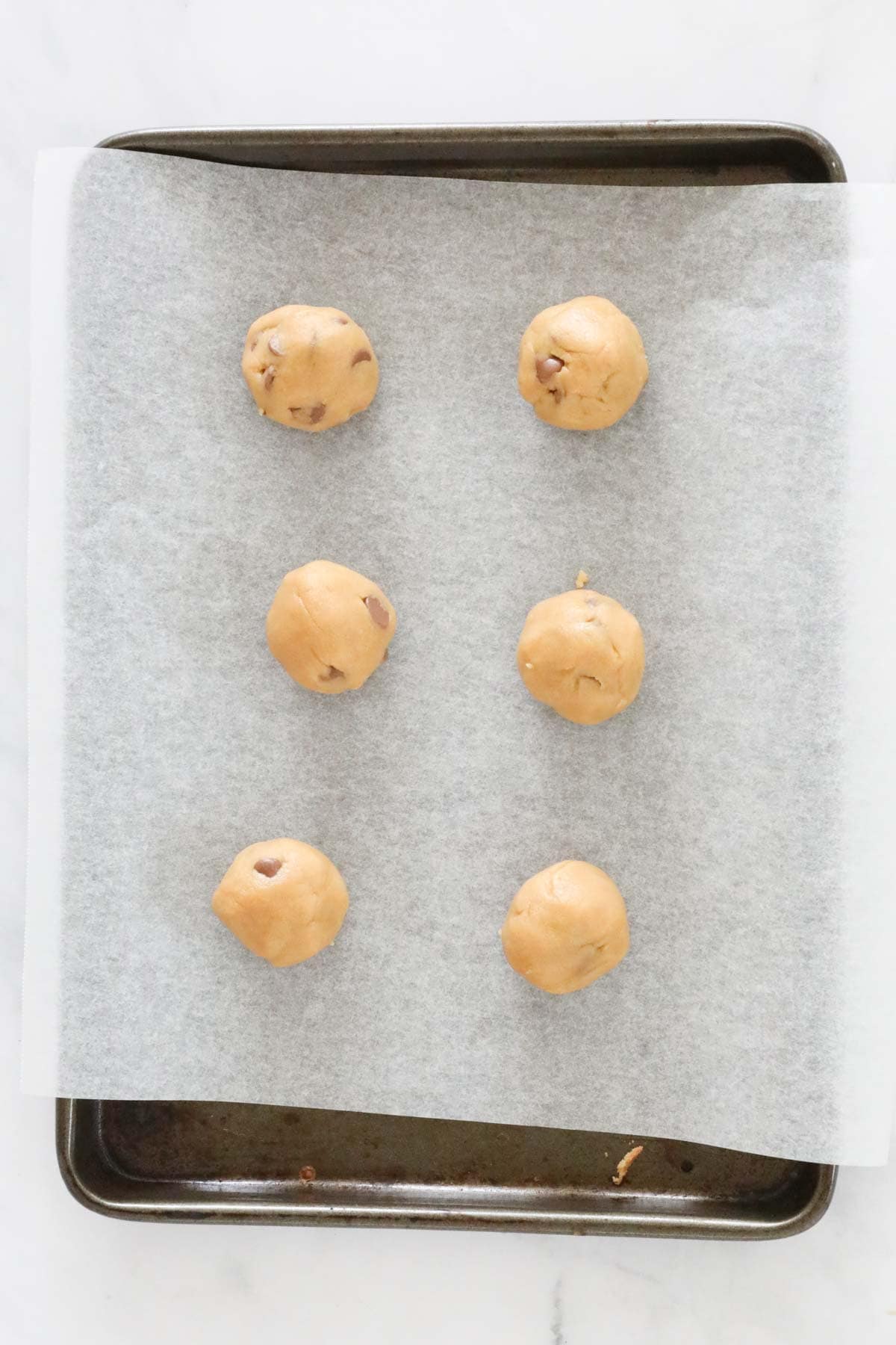 Balls of cookie dough placed on baking tray lined with baking paper.